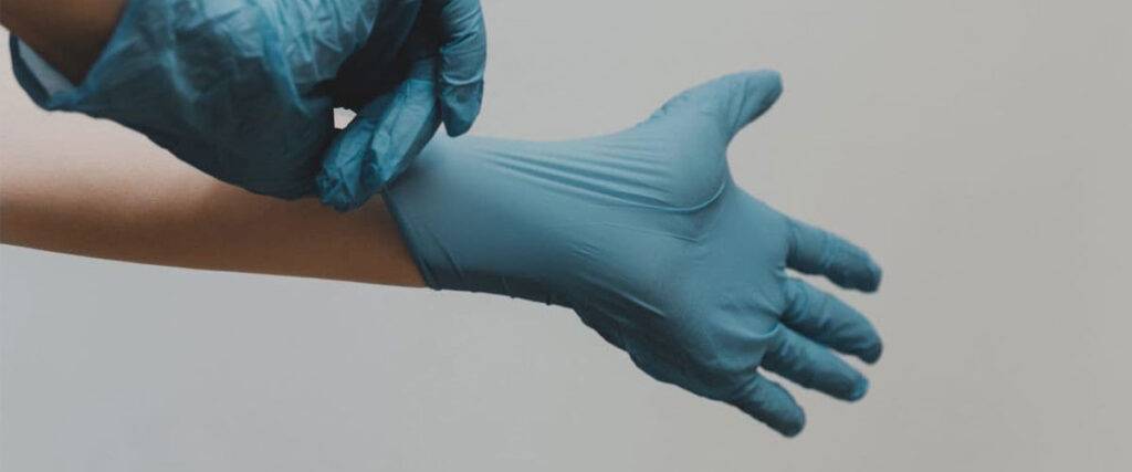 فردی در حال دست کردن دستکش پزشکی آبی رنگ.